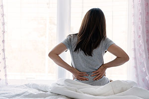 Woman sitting in bed holding her back